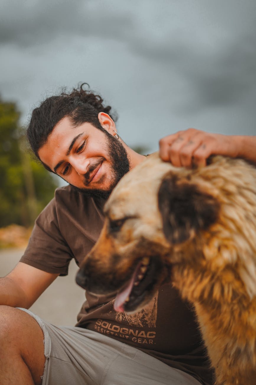 a man in brown shirt smiling while petting his dog